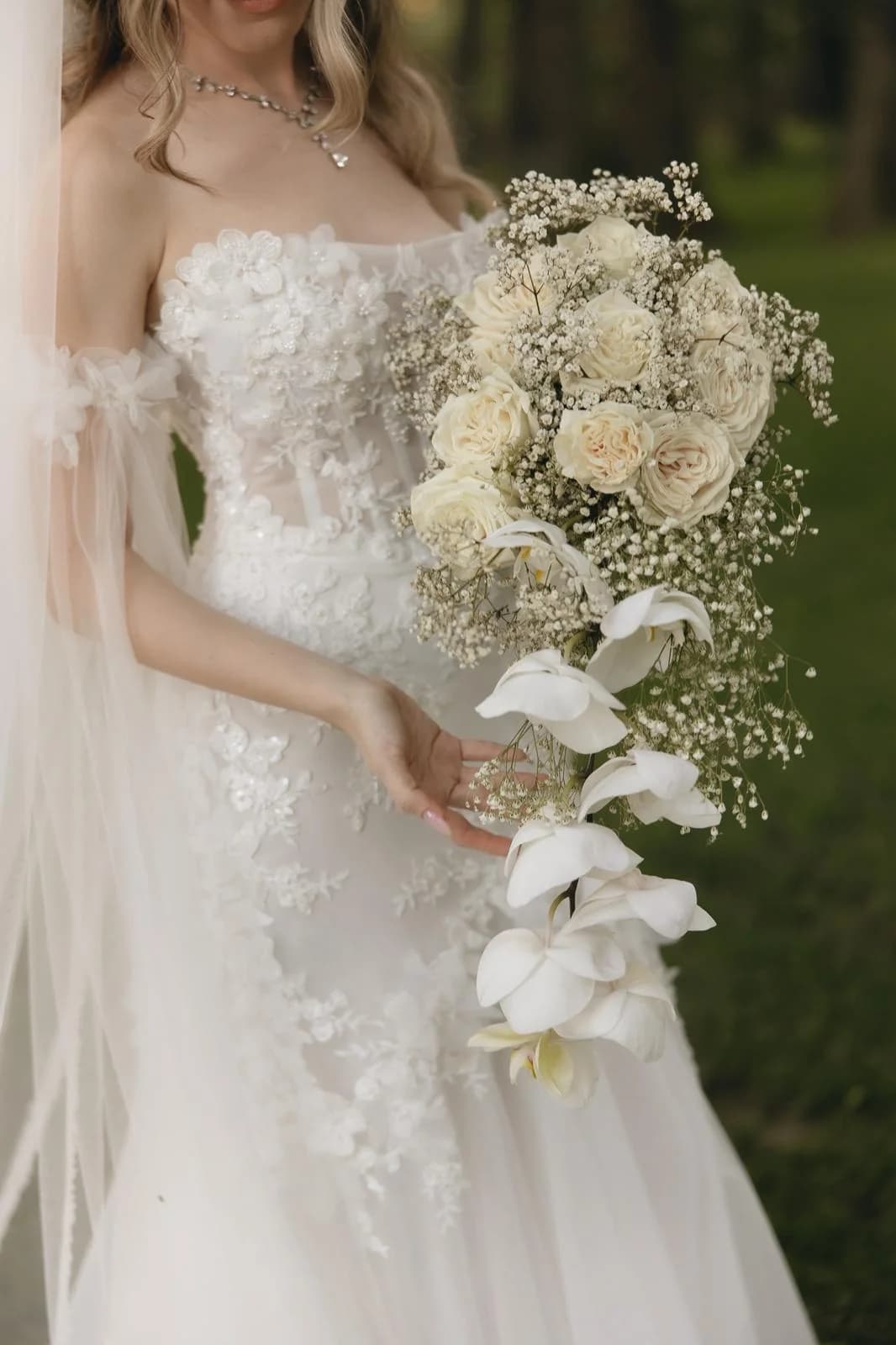 Mireasă cu un buchet cascadă din trandafiri crem, gypsophila și orhidee albe